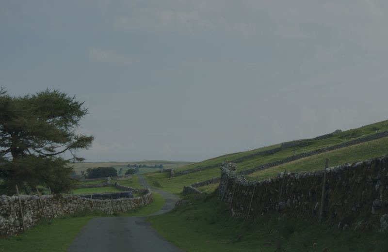 A quiet Lake District lane between dry stone walls, fells rising beyond, on the walking country that shaped Wordsworth and Coleridge