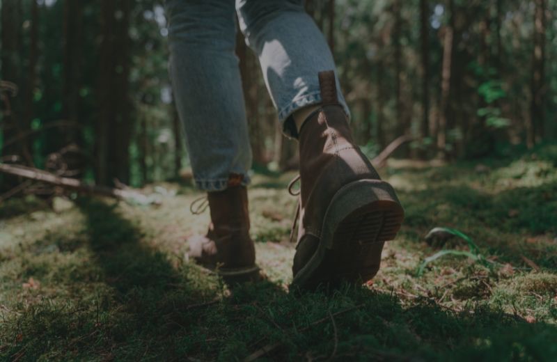 Walking boots and jeans mid-step through sunlit woodland, moss underfoot, the slow pace of a morning taken walking